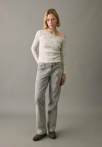 Vaaleanharmaa teksturoitu neulepusero, jossa on olkaimeton malli, yhdistettynä harmaisiin farkkuihin, joissa on sivusaumat ja väljät istuvuus. Ruskeat nilkkurit.