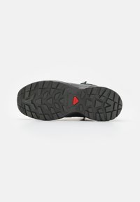 Suela de zapato exterior negra con un patrón de textura y un acento rojo cerca del talón, diseñada para proporcionar tracción y estabilidad.