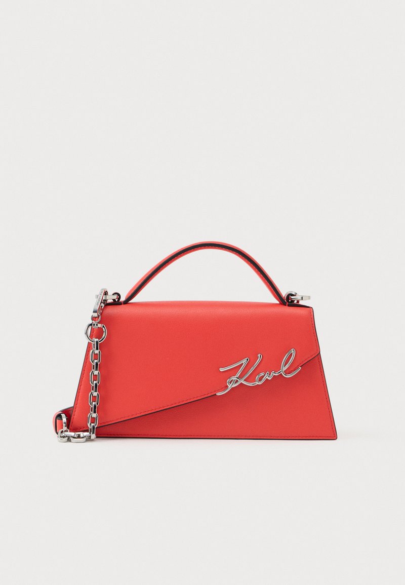 Red leather handbag with a structured design, metal chain strap, and a silver logo accent. Smooth texture and angular shape.
