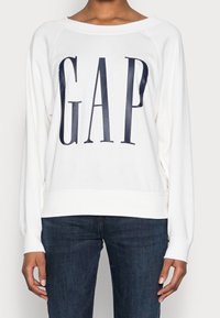 Felpa bianca con logo "GAP" blu navy, vestibilità rilassata, maniche raglan, orlo e polsini ribattuti, tessuto morbido con una texture liscia.
