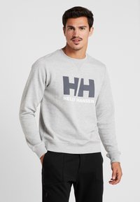 Sudadera gris hecha de una tela suave, con un gran logo en azul oscuro "HH" y texto blanco que dice "HELLY HANSEN" en la parte frontal.