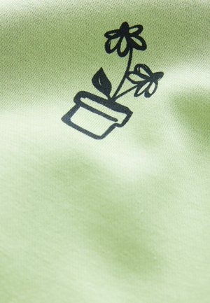 Černá linie umění potted rostliny se dvěma květinami na měkkém, světle zeleném textilním pozadí. Design je umístěn uprostřed a je jasný.