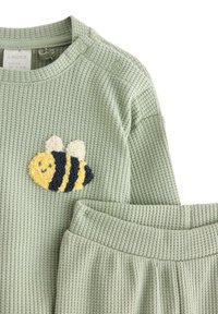 Completo per bambini di colore verde con texture a wafer, comprende una maglietta con un'applicazione di un'ape gialla e blu navy e un pantalone coordinato a vita elastica.