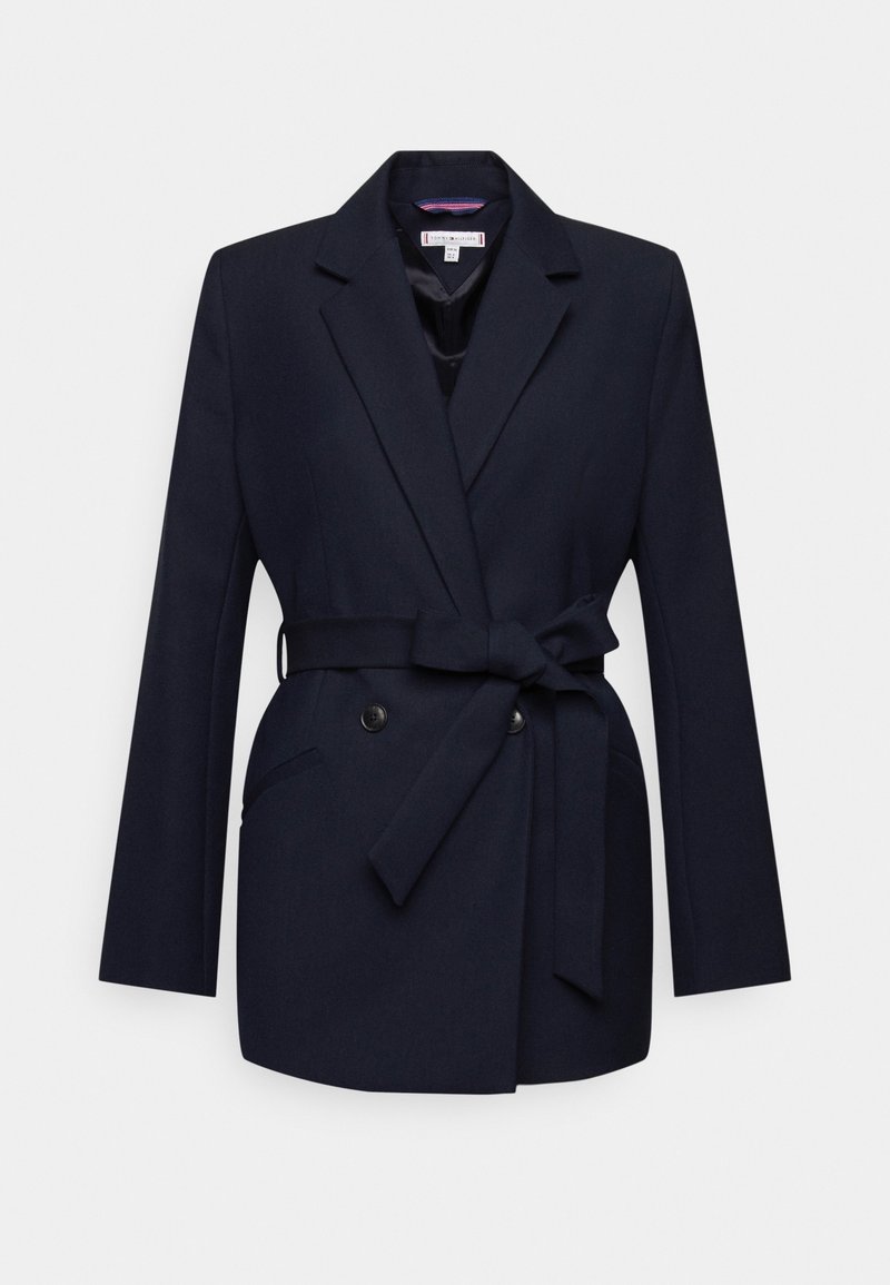 Granatowa marynarka o dopasowanym kroju, z podwójnymi guzikami, bocznymi kieszeniami i związanym w pasie paskiem. Gładka faktura materiału.