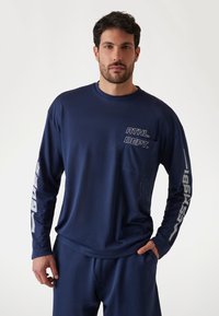 Marineblauw sportshirt met lange mouwen, gemaakt van gestructureerde stof, met "ATHL. DEPT." gedrukt op de voorkant en "1981" langs de mouw.