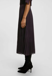 Pitkä laskostettu mekko tummanvioletissa, puoliläpinäkyvällä tekstuurilla, jossa on lyhyet hihat ja asustettuna istuvilla mustilla nilkkureilla.