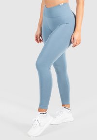 Lichtblauwe, aansluitende leggings van rekbaar materiaal, met een hoge tailleband. Gecombineerd met witte sportschoenen. Soepele textuur.