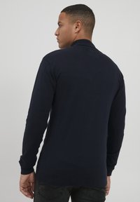 Pull-over à manches longues bleu marine avec un col et des poignets côtelés, présentant une texture lisse et un design uni sans motifs ni accents visibles.
