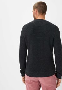 Donkergrijs gebreid sweatshirt met lange mouwen en een ronde hals, met een gestructureerd oppervlak en ribgebreide manchetten. Draagt het met lichtroze corduroy broek.