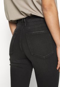 Svarta denimjeans med hög midja, med bakfickor och slät textur, kombinerat med en lös beige toppen.