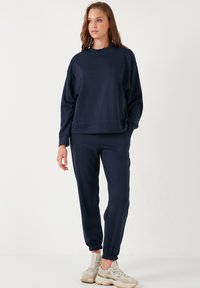 Tengerészkék pulóver és jogger szett. Puha anyag, laza illeszkedés, bordázott mandzsetták a csuklóknál és bokáknál, valamint oldalsó zsebek a joggernél. Kényelmes kialakítás.