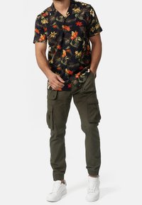 Svart t-shirt med kort ärm och livfullt blommönster, i kombination med olivgröna cargobyxor med sidofickor och elastiska ärmslut, som bärs med vita sneakers.