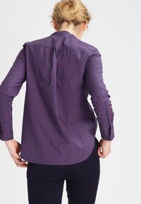 Chemise à carreaux marine et rouge avec des manches longues, un ourlet arrondi et un col boutonné. Tissu texturé avec patte de boutonnage et boutons aux poignets.