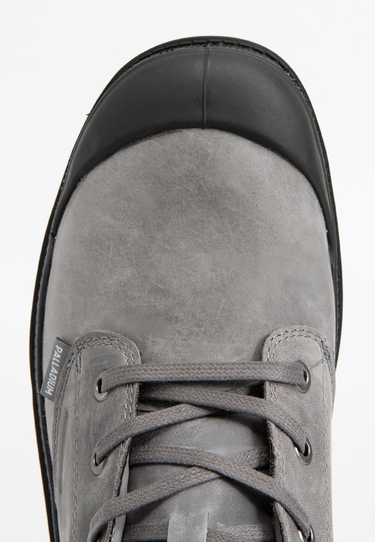 Szare zamszowe buty z czarnym gumowym noskiem, okrągłymi sznurówkami i metalowymi oczkami. Charakteryzują się fakturowaną powierzchnią i przeszyciami.
