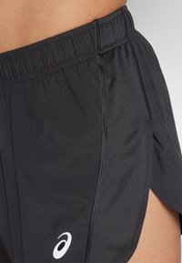 Black athletic shorts with an elastic waistband, side slit design, and a white logo. Smooth texture with breathable fabric.