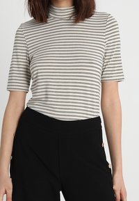 Top de manga corta a rayas en crema y negro, con un cuello alto y fabricado en una tela suave, combinado con pantalones negros con detalles de botones dorados.