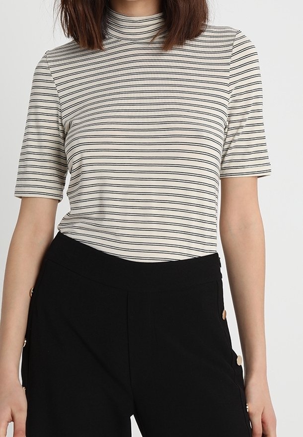 Top de manga corta a rayas en crema y negro, con un cuello alto y fabricado en una tela suave, combinado con pantalones negros con detalles de botones dorados.