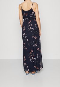 Marinblå maxiklänning med tunna axelband, med rosa och vita blommönster, lättviktsmaterial och dräppt midja.