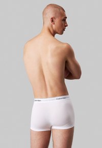 Hvide bomulds boxershorts med en sort Calvin Klein elastik, vist på en model set fra ryggen, som fremhæver en glat og tætsiddende form.