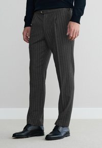 Gray pinstriped trousers made of a smooth fabric, featuring a tailored fit, two front pockets, and a button closure at the waistband.
