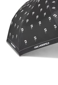 Čierny dáždnik s opakovaným vzorom bielych lebiek, s bielym lemom a značkou "KARL LAGERFELD" pozdĺž okraja.