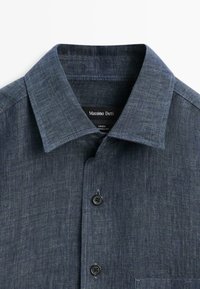 Ciemnoniebieska lniana koszula na guziki z ostro zakończonym kołnierzem i metką Massimo Dutti wewnątrz kołnierza.