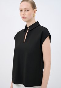 Top senza maniche nero con colletto e dettaglio a chiave sul davanti. Realizzato in tessuto liscio, presenta un design minimalista e linee pulite.