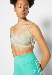 Sutiã desportivo em camuflagem nas cores púrpura clara e verde, com alças finas. Combinado com leggings turquesa de cintura alta com três riscas brancas.