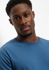 Maglietta blu a girocollo che mette in risalto un tessuto liscio e leggero con una vestibilità aderente, mostrando una texture sottile e un design pulito e semplice.