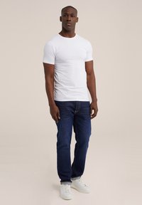 Witte katoenen T-shirt met korte mouwen, gecombineerd met donkerblauwe jeans en witte sneakers. Eenvoudig ontwerp, geen zichtbare patronen of logo's.