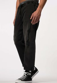 Joggers de denim negro con cintura elástica, detalles desgastados y pierna ajustada. Combinados con zapatillas altas negras y cordones blancos.