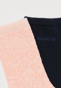 Ζευγάρι κάλτσες, μία ροζ με λεοπάρ σχέδιο και μία μονόχρωμη σκούρο μπλε, και οι δύο με το όνομα της μάρκας "Hugo" κοντά στο μανσέτα.