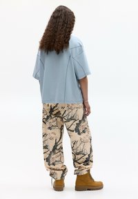 Světle modré oversized tričko s krátkým rukávem, doplněné béžovými vzorovanými kalhotami s černými větvemi a růžovými květy. Hnědé šněrovací boty.