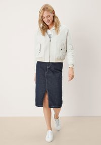 Witte bomberjack met geribbelde zoom en twee voorzakken, gecombineerd met een donkerdenim midirok met een voorkapslits. Witte sneakers maken de look compleet.