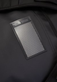 Black nylon backpack interior featuring a transparent hexagonal-patterned pocket with a black trim and "THE NORTH FACE" branding.