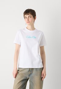 Hvit bomulls T-skjorte med korte ermer, med en lys blå "Calvin Klein" logo brodert på brystet. Casual, avslappet passform.