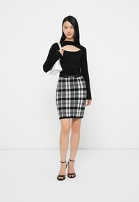 Μαύρη μπλούζα με μακριά μανίκια και λεπτομέρεια κοπής, συνδυασμένη με μια εφαρμοστή καρό φούστα σε γκρι και μαύρο, με μια φαρδιά μαύρη ζώνη. Μαύρα πέδιλα με λουράκια.