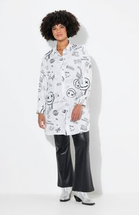 Chemise blanche avec des imprimés graphiques noirs, design à boutons, manches longues, associée à un pantalon noir évasé et des bottes chelsea argentées.