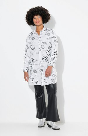 Chemise blanche avec des imprimés graphiques noirs, design à boutons, manches longues, associée à un pantalon noir évasé et des bottes chelsea argentées.