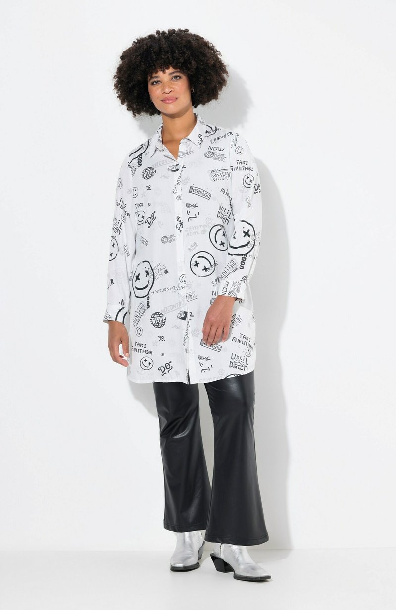 Chemise blanche avec des imprimés graphiques noirs, design à boutons, manches longues, associée à un pantalon noir évasé et des bottes chelsea argentées.