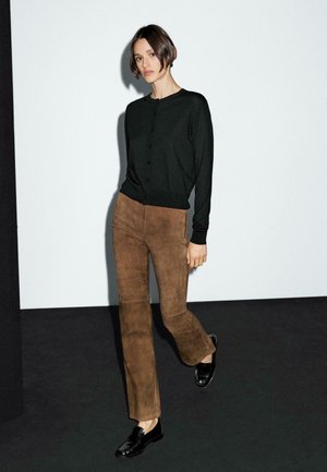 Sort cardigan med lange ærmer og knapper, kombineret med brune flared bukser i ruskind og sorte læderloafers, placeret mod en minimalistisk baggrund.