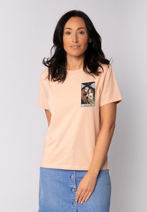 T-shirt en coton pêche à manches courtes, avec un imprimé graphique sur la poitrine représentant un couple, dessiné en couleurs sombres.