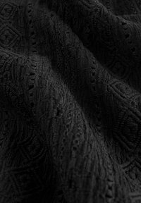 Schwarzer Textilstoff mit komplexen Mustern, der erhabene Designs und eine weiche, plüschige Oberfläche aufweist. Ideal für Polsterungen oder Bekleidung.