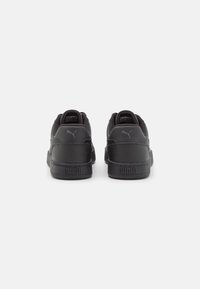 Schwarze Sneaker mit einem glatten Lederoberteil, gepolstertem Schaft und Gummisohle; dezente Logo-Akzentuierung an der Ferse.