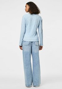 Camicia a maniche lunghe azzurro chiaro con un sottile motivo floreale, abbinata a jeans larghi azzurri chiari. Tessuto morbido; taglio rilassato.
