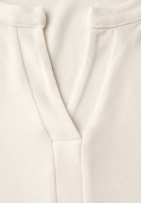 Weißes Oberteil aus Stoff mit V-Ausschnitt, glatter Textur und subtiler Rippung entlang des Ausschnitts und der Knopfleiste.