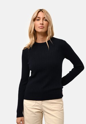 Maglione a coste di colore blu navy con maniche lunghe e scollo rotondo, abbinato a pantaloni chiari. Texture liscia e design aderente.