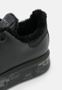 Baskets noires avec doublure en fourrure douce, accents cousus et semelle imprimée avec texte et motifs graphiques abstraits.