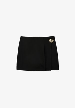 Minifalda negra con una tabla frontal y un pequeño pasador decorativo dorado en la cadera derecha.