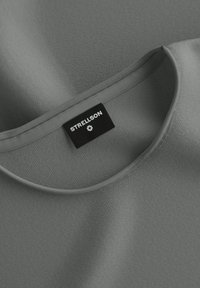 Graues Stoff-T-Shirt mit glatter Textur, das einen runden Ausschnitt aufweist und ein schwarzes Etikett mit weiße Schrift und Symbol auf der Innenseite hat.